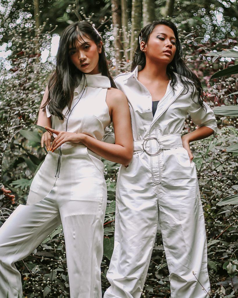 Fashion models posing in stylish jumpsuits amidst tropical greenery.