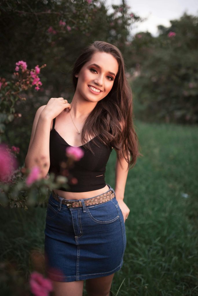 Charming young woman smiling in a natural garden setting during daytime.