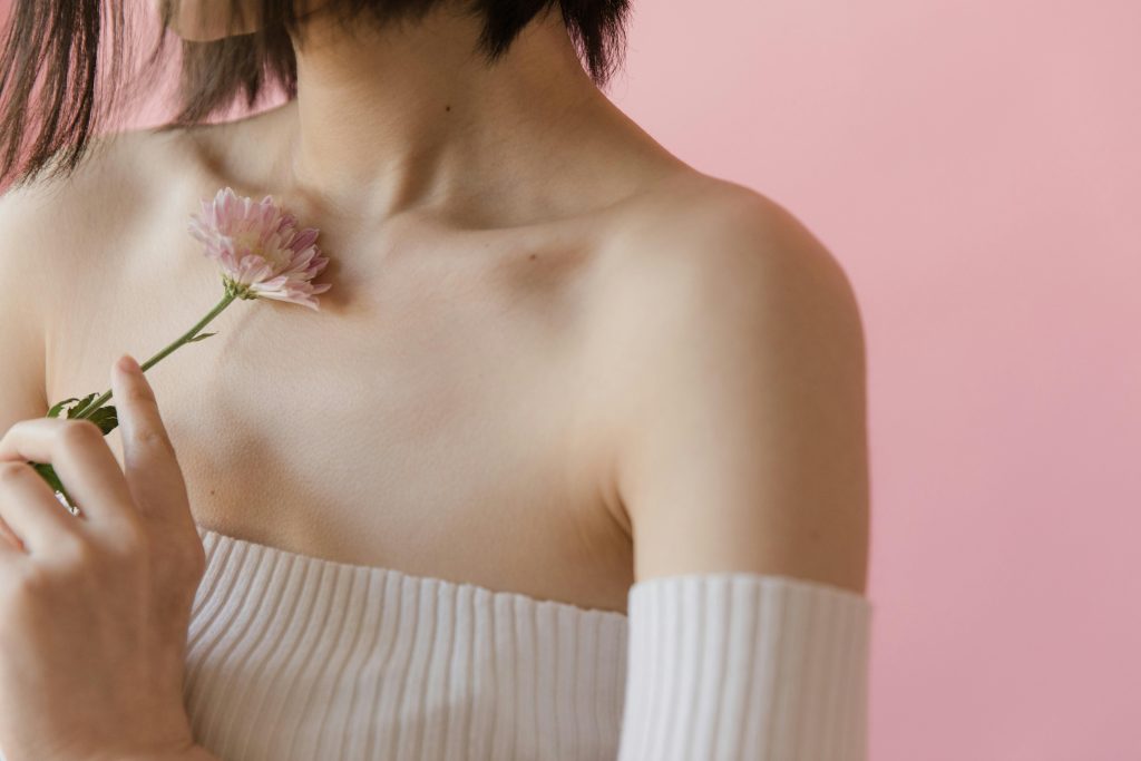 A serene close-up image of a woman holding a pink flower against a pastel background.