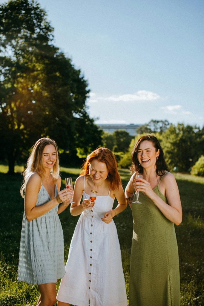 Three women joyfully celebrate outdoors with champagne under sunny skies.