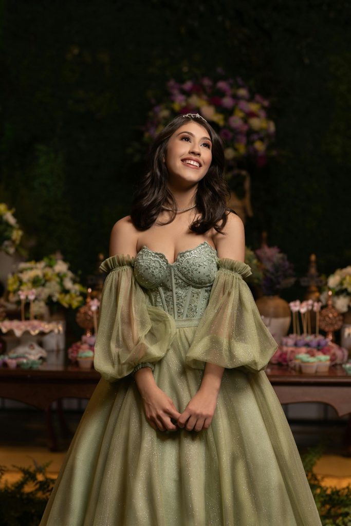 A teenage girl smiling in a luxurious green dress during her quinceañera celebration.