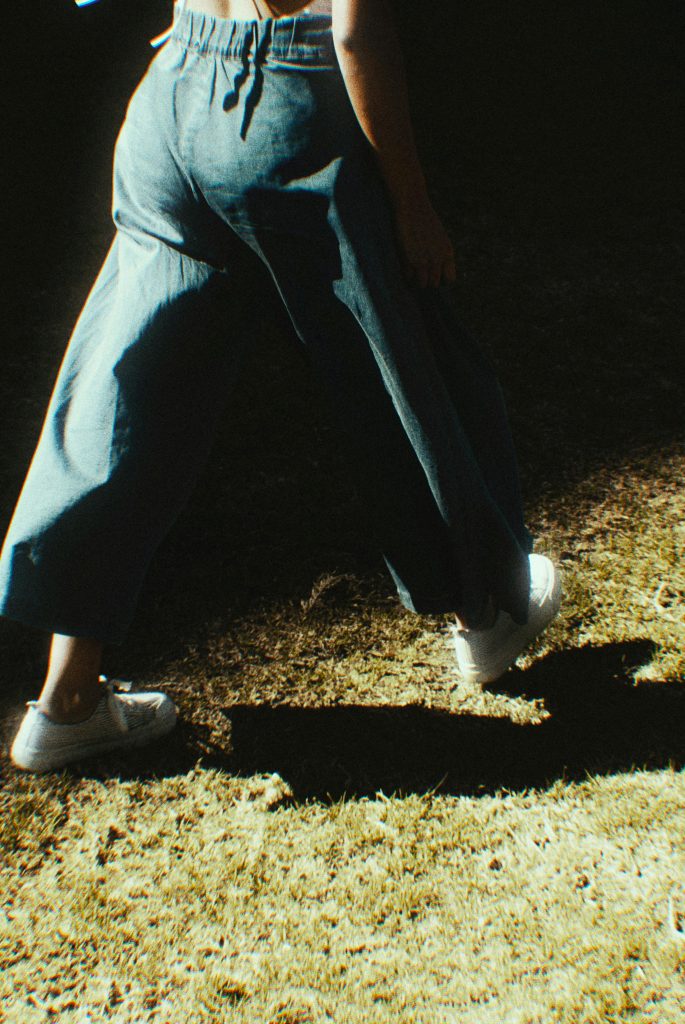 A person walks casually in denim jeans, casting a shadow on a sunlit path.