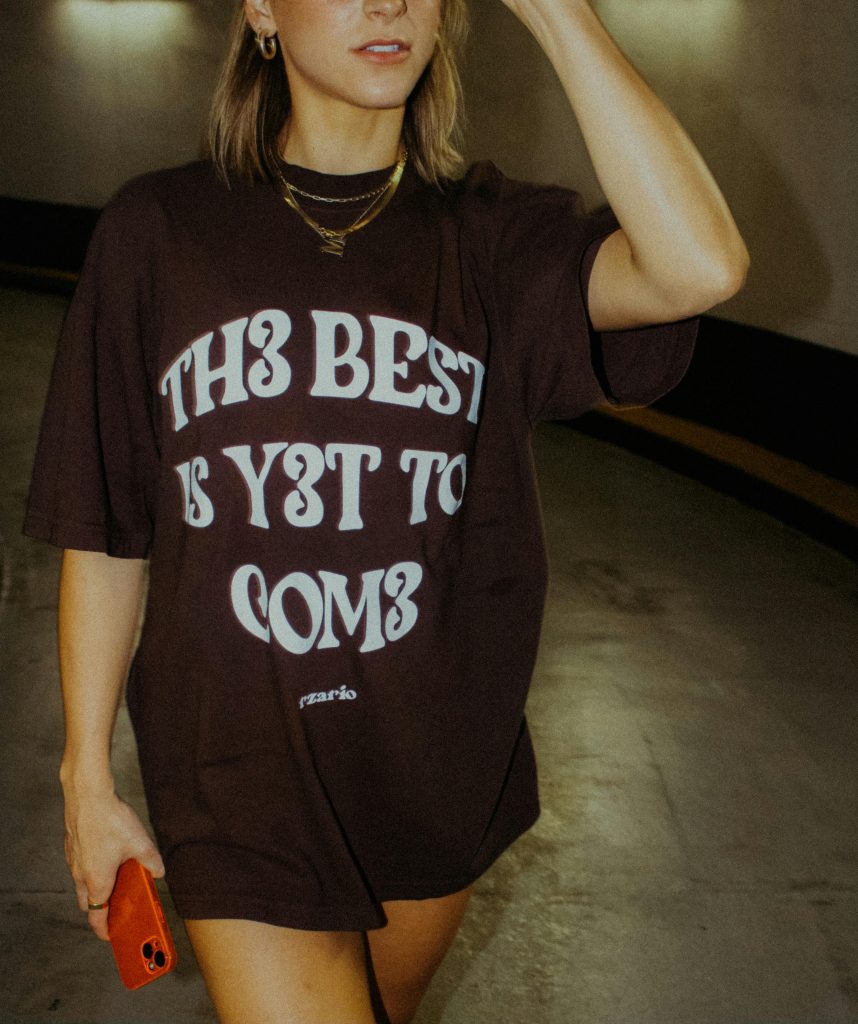 Woman in oversized graphic t-shirt holding a smartphone in a stylish urban location.