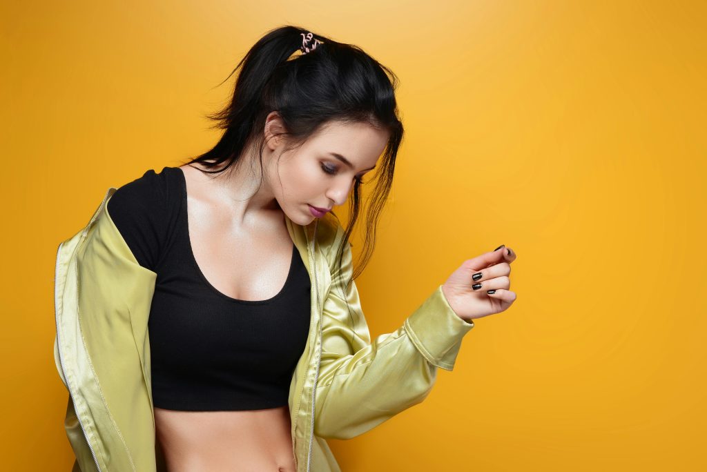 Stylish woman poses confidently in a black crop top and satin jacket, set against a vibrant yellow background.