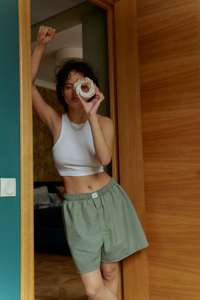 Casual scene of a woman holding a donut, posing playfully in a doorway, wearing comfortable indoor attire.