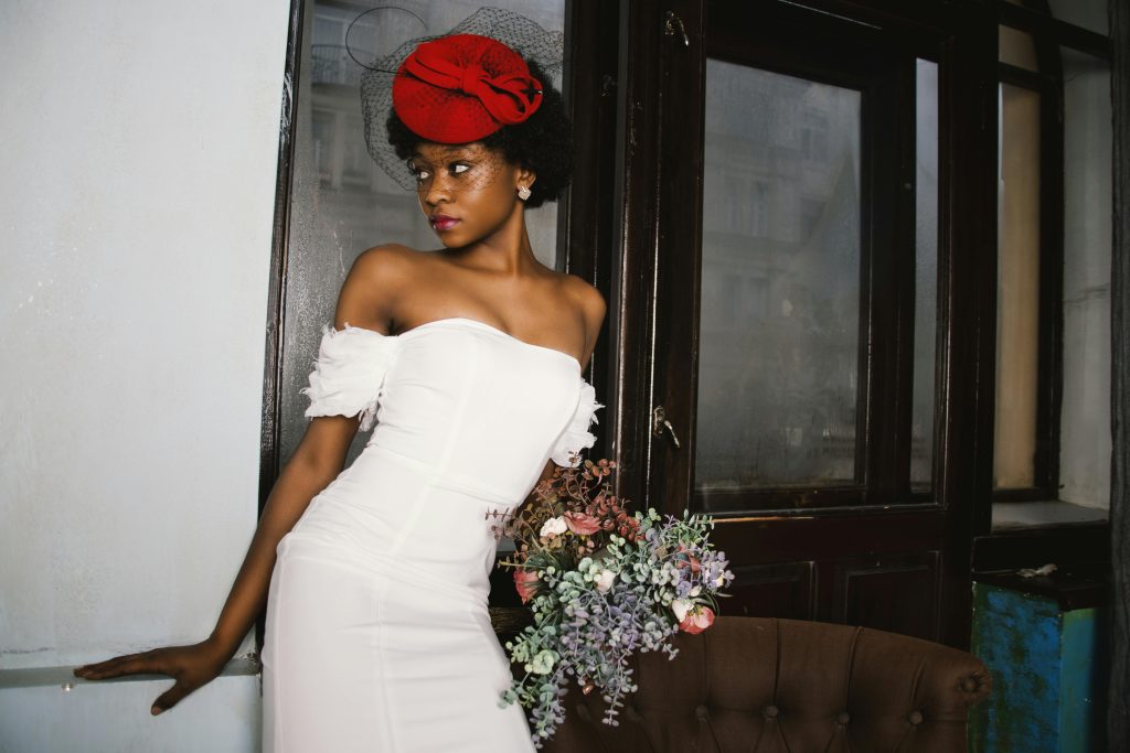 Stunning bridal portrait of an elegant bride in a white dress with a red hat indoors.