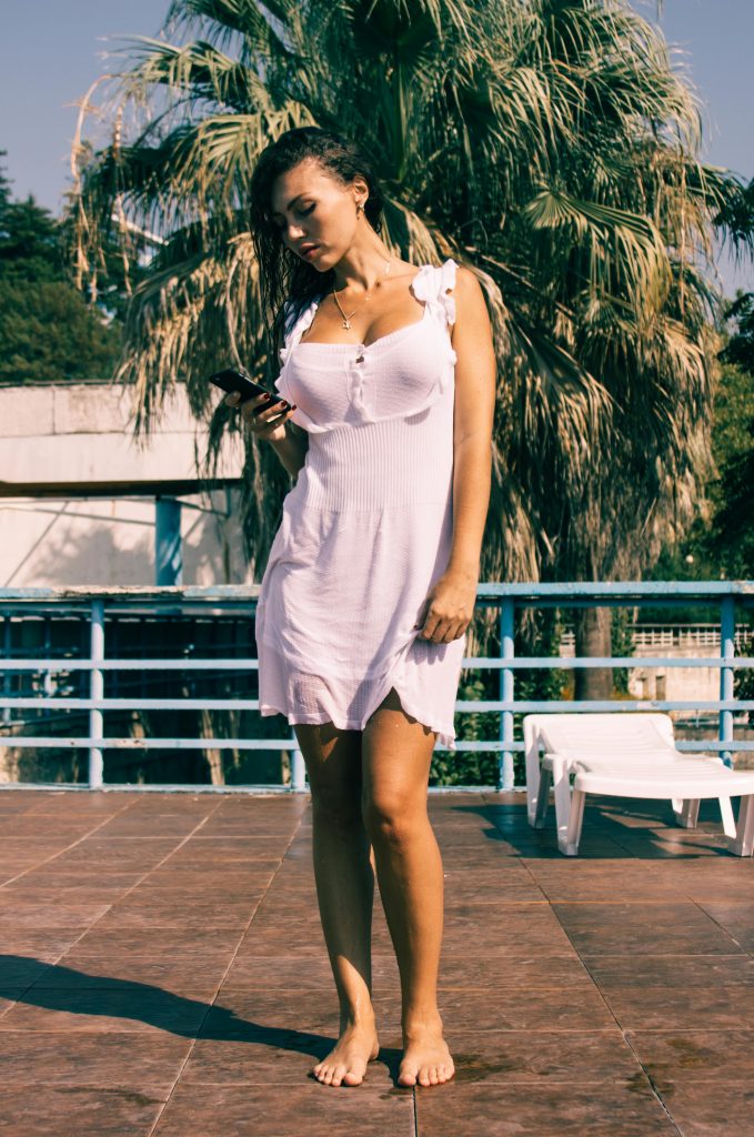 A woman in a white summer dress standing by a poolside, enjoying sunny weather.